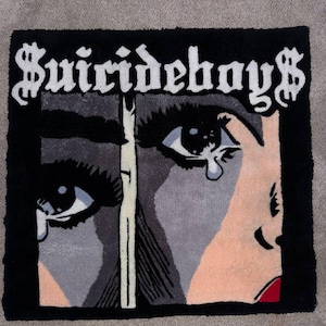 Puede incluir: Una alfombra negra y gris con una ilustración de estilo pop art de una cara con lágrimas. La palabra "Suicideboys" está escrita en blanco, con una tipografía estilizada sobre la cara. La cara está dividida en dos secciones.