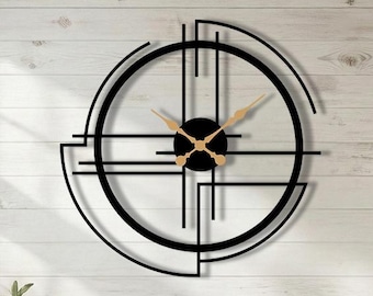 May include: A large, black, geometric wall clock with gold-colored hands and a black center. The clock is mounted on a white wooden wall in a living room setting. The clock's design features intersecting lines and a circular shape.