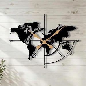 Pode incluir: Relógio de parede de mapa-múndi em metal preto com ponteiros dourados e design de bússola. O relógio está montado em uma parede de madeira branca, adicionando um toque decorativo ao ambiente. O design do relógio inclui os continentes e uma rosa dos ventos.