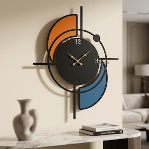 Puede incluir: Un reloj de pared negro con un centro circular, manecillas doradas y los números 3, 6 y 12. El marco incluye líneas geométricas negras, un acento semicircular naranja en la parte superior izquierda y un acento azul en la parte inferior derecha.
