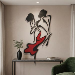 May include: A black metal wall art piece depicting two figures in a dancing pose, with one figure wearing a flowing red dress. The design features clean, continuous lines and minimalist silhouettes, creating a dynamic sense of movement.