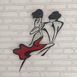 May include: A black metal wall art piece depicting two stylized figures in a dancing pose. The figure on the left wears a flowing red dress, while the figure on the right is rendered in solid black lines. The design features smooth, curved contours.