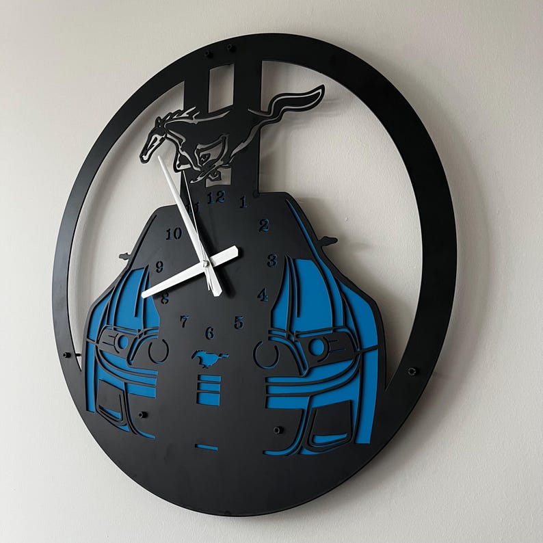 May include: Black and blue wall clock featuring a car design with a running horse silhouette. The clock has white hands and a circular black frame. The clock measures approximately 12 inches in diameter.