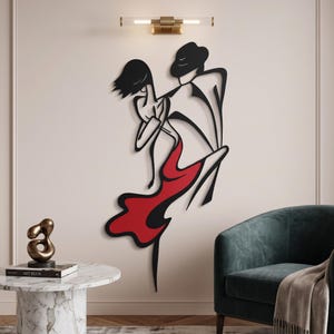 May include: A black metal wall art piece depicting a stylized couple dancing, featuring a figure in a hat and a figure in a flowing dress with a prominent red section. The design uses bold, continuous lines to create a fluid, abstract silhouette.