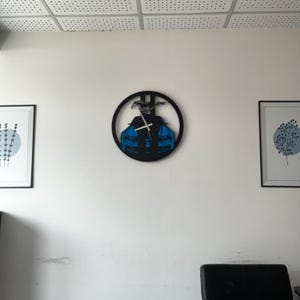 May include: A black wall clock featuring a blue sports car design. The clock has a circular shape with a car silhouette and a horse emblem. The clock hands are white, and the clock is mounted on a white wall.