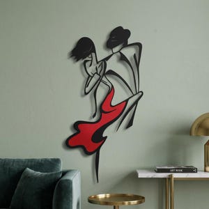 May include: A black metal wall art piece depicting two figures in a dance pose. The male figure is outlined in black, while the female figure features a solid red dress section. The design uses clean, continuous lines to form the silhouettes.