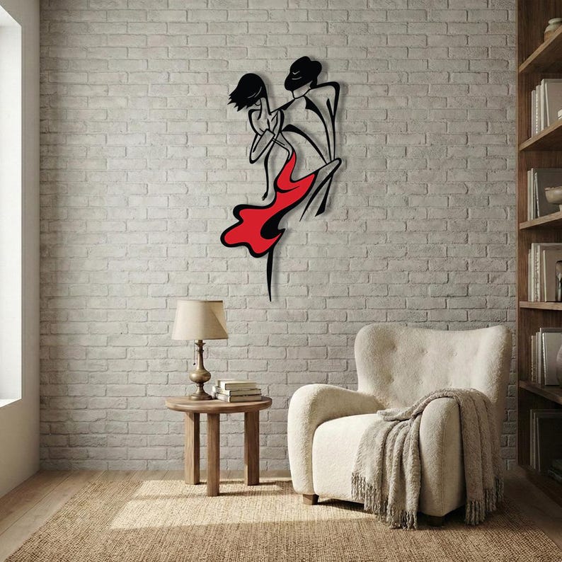 May include: A black metal wall art piece depicting a stylized couple dancing, featuring a bold red dress on the female figure. The design uses clean, continuous lines to outline the silhouettes of the two figures in a dynamic, flowing pose.