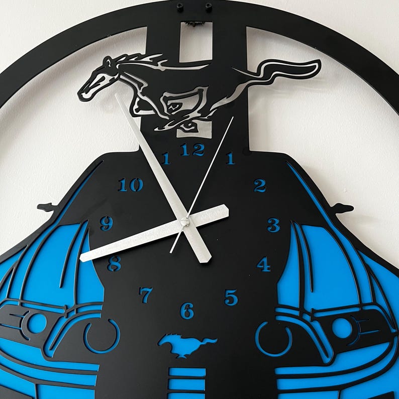 May include: Black and blue wall clock featuring a running horse silhouette. The clock has a car-shaped design with blue accents and silver clock hands. The numbers are in a blue font. The clock is a decorative item.