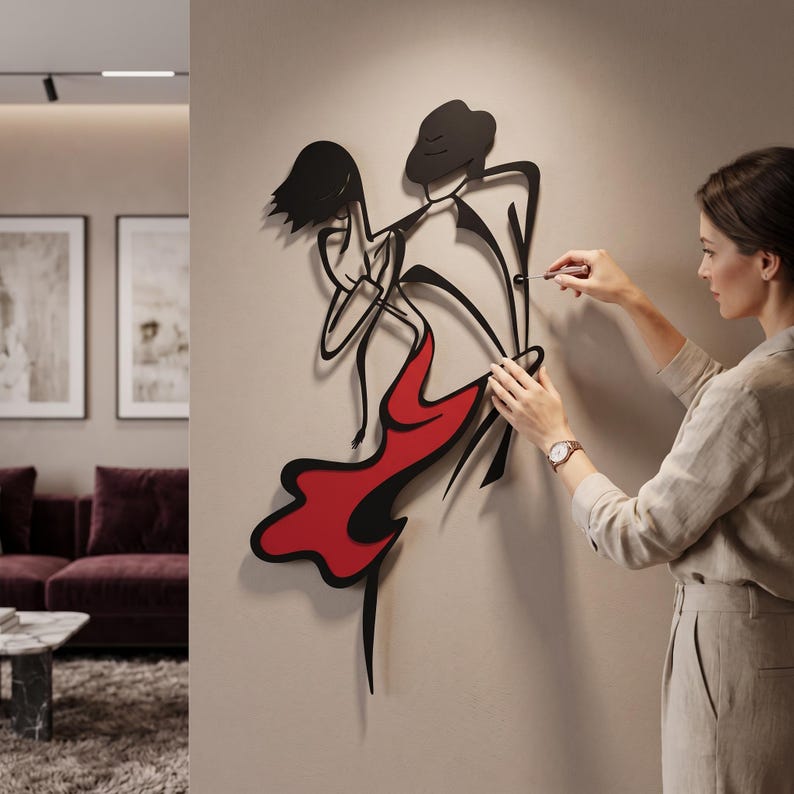 May include: A black metal wall art piece depicting a stylized dancing couple. The design features a figure in a hat and a figure in a flowing dress with a solid red accent section. The sculpture is composed of thin, continuous lines forming silhouettes.