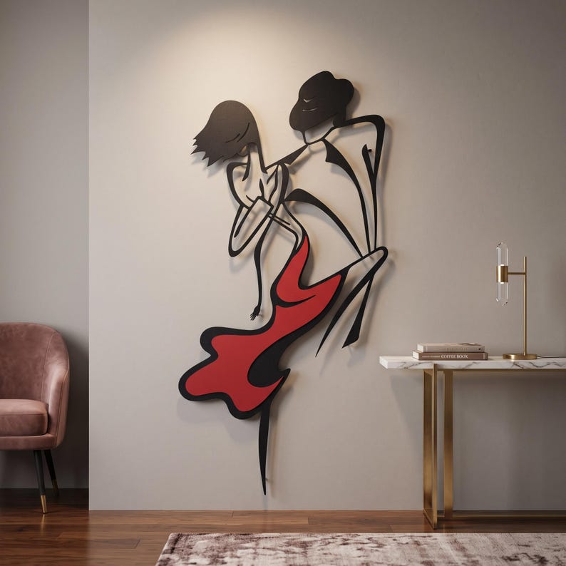 May include: A black metal wall art sculpture depicting two figures in a dynamic dancing pose. The female figure wears a flowing red dress, while the male figure is rendered in solid black lines. The piece is mounted on a plain wall surface.