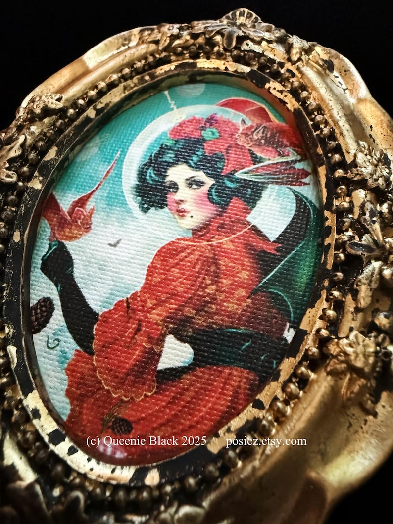 Op de afbeelding: Een ingelijst schilderij van een vrouw met donker haar en een rode jurk. Ze houdt een rode vogel in haar hand. De achtergrond is een blauwe en groene lucht met een maan. De lijst is goud en versierd. De tekst (c) Queenie Black 2025 posiez.etsy.com is zichtbaar onderaan de afbeelding.