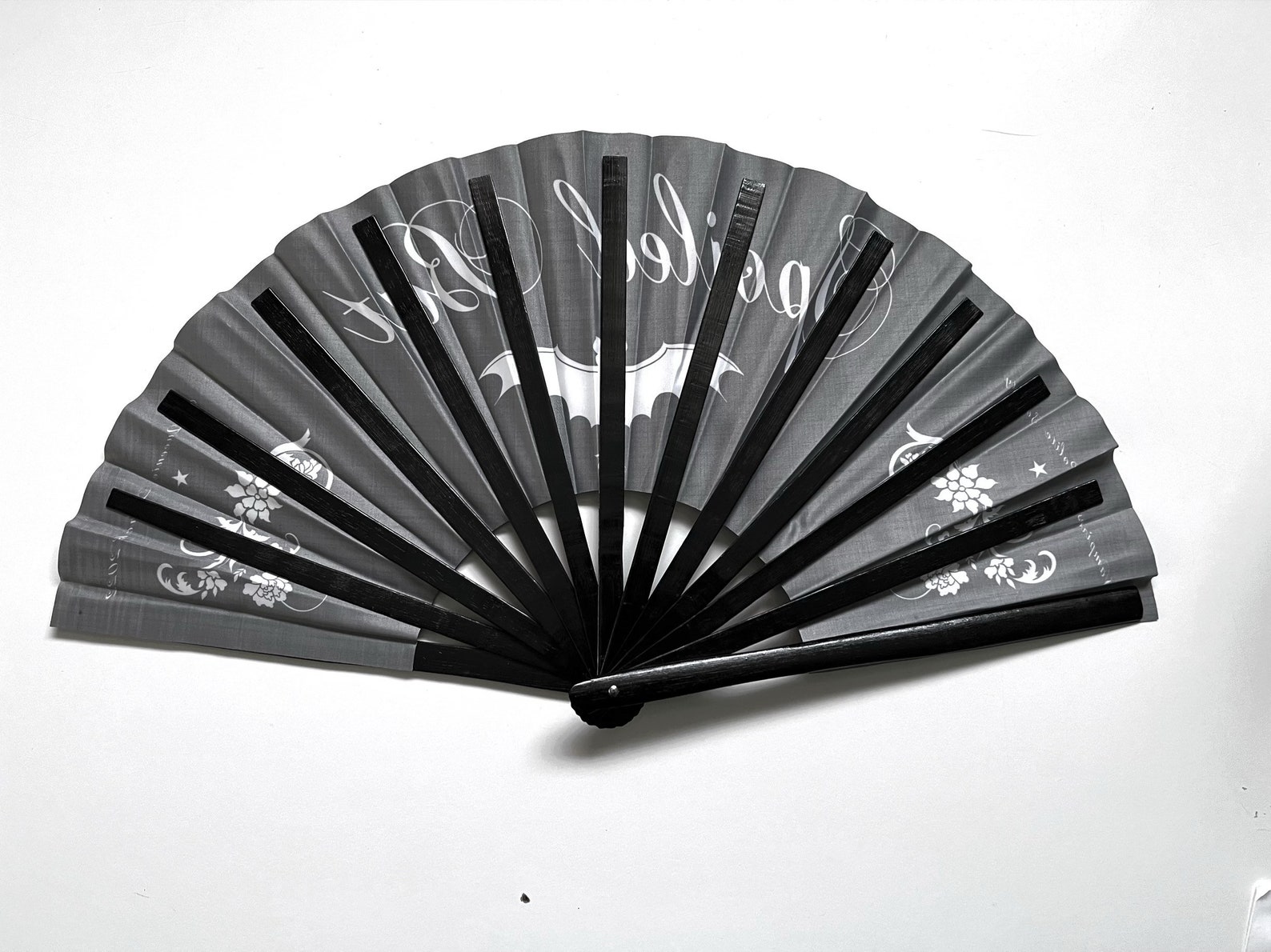 Partially closed black gothic fan showing white bat motif, floral accents, and the word “Spoiled” in decorative script.