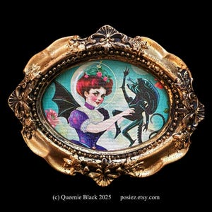 May include: A framed illustration of a woman with red hair and a bat-like wing, holding a small, black, alien-like creature. The background is a turquoise blue with a moon and stars.