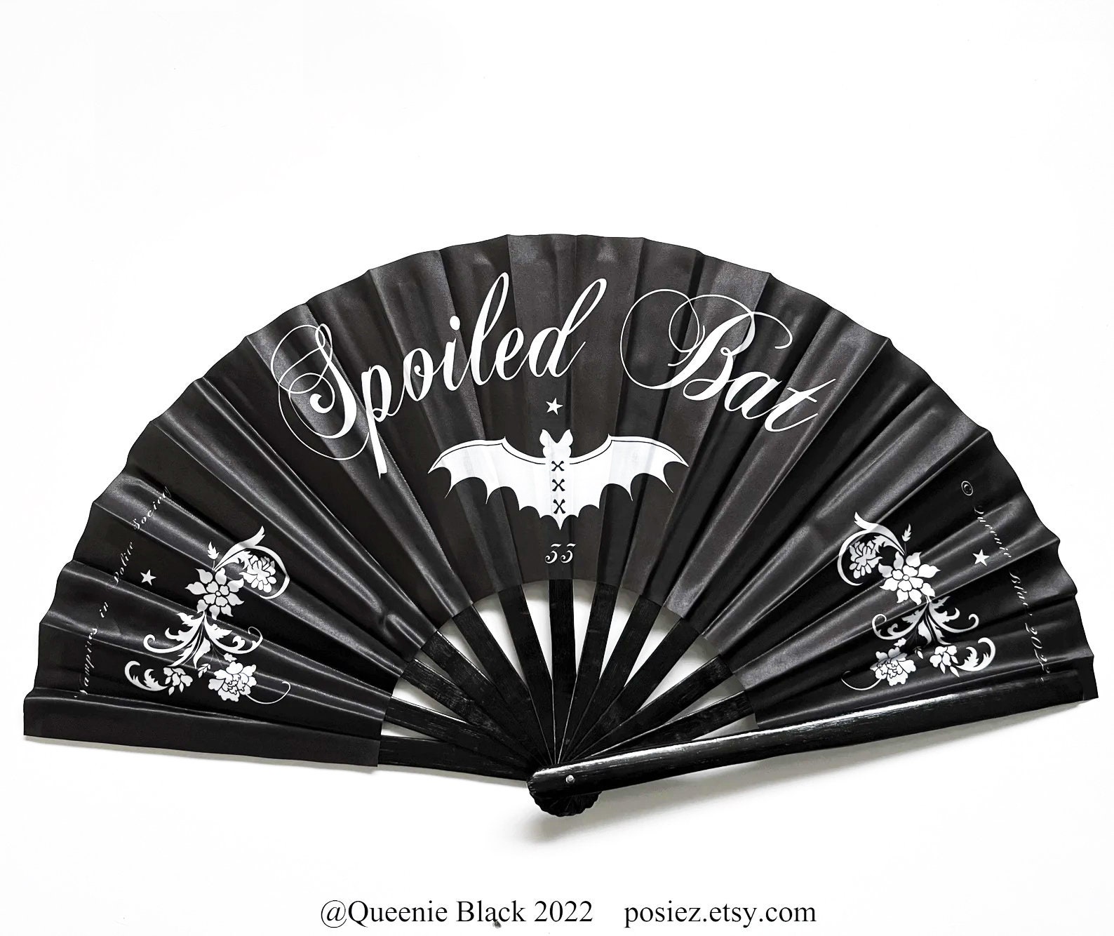 Black gothic folding fan with white “Spoiled Bat” text, bat graphic, and floral scroll accents on each side.