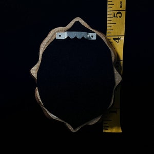 May include: A wooden frame with a scalloped edge and a black velvet backing. The frame has a metal hanger on the back.