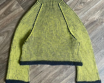 May include: A long-sleeved sweater featuring a high mock neck and a vertical ribbed knit pattern. The garment is primarily lime green with dark navy blue trim along the collar, the hemline, and the edges of the wide, flared sleeves.