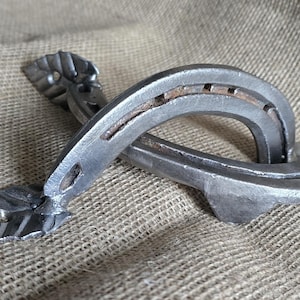 May include: A silver metal door handle with a horseshoe design and leaf-shaped accents.