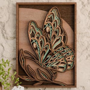Könnte beinhalten: Wandkunst aus Holz mit einem Schmetterling im geschichteten Design. Der Schmetterling weist aufwendige Ausschnitte auf und ist in Braun- und Türkistönen bemalt. Das Kunstwerk ist in einem rechteckigen Holzrahmen montiert.