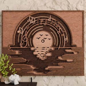 May include: Wooden wall art showing a sunset scene with a vinyl record design. The artwork has a layered design with musical notes, birds, and water reflections. The colour palette includes shades of brown and tan.