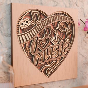 May include: A layered wooden art piece in the shape of a heart, featuring musical elements. The design includes musical notes, a piano keyboard, a cassette tape, and the words "I ❤️ MUSIC". The artwork is in shades of brown and beige.