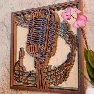 May include: A layered wooden wall art piece featuring a vintage microphone design. The artwork incorporates musical notes and a treble clef, with brown, teal, and cream colors. The piece is framed in a dark brown border.