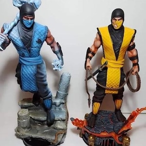 Puede incluir: Dos figuras de acción de personajes de Mortal Kombat. Una figura es azul y negra, sosteniendo un arma de hielo. La otra es amarilla y negra, sosteniendo una cuerda y una espada. Figuras sobre bases.