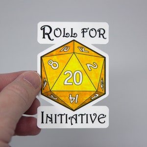 May include: A white sticker with the text "Roll for Initiative" and a yellow 20-sided die with black numbers.