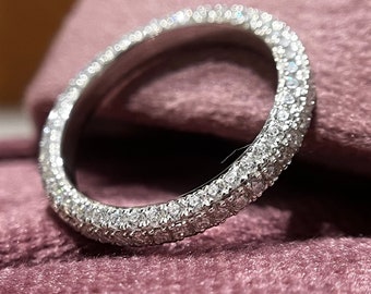 May include: A silver band ring with a double row of small, clear diamonds set in a pave setting. The ring is on a pink velvet surface.