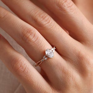 May include: A delicate engagement ring featuring a central oval-cut diamond. The ring has a slender band with intricate detailing and smaller accent stones. The design is elegant and classic, perfect for a special occasion.