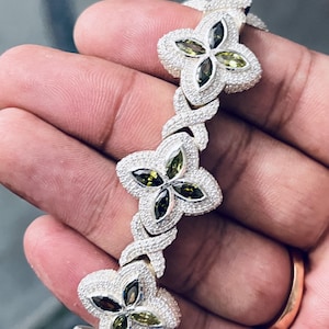 May include: A silver bracelet with a chain link design and green and white gemstones set in a flower shape.