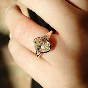 May include: A rose gold ring featuring a large oval-shaped diamond set in a bezel setting. The diamond has a slight yellow hue.