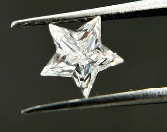 May include: A clear, faceted star-shaped diamond held by tweezers. The diamond is cut into a star shape with many facets.