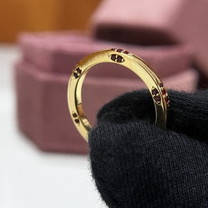May include: A gold band ring with a row of small red gemstones set into the band.