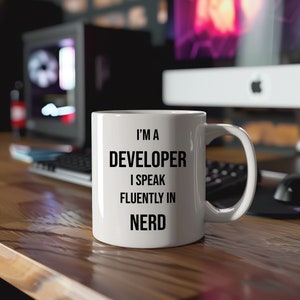 May include: White ceramic coffee mug with black text that reads "I'm a Developer I speak fluently in Nerd".