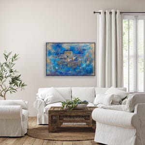 Puede incluir: Una pintura abstracta enmarcada que representa un edificio con una c&uacute;pula dorada, rodeado de un patr&oacute;n de remolinos azules y blancos. La pintura est&aacute; colgada en una pared blanca sobre un sof&aacute; blanco.