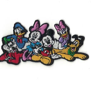 Op de afbeelding: Een geborduurde patch met Mickey Mouse, Minnie Mouse, Donald Duck, Daisy Duck en Goofy. De personages lachen allemaal en lijken samen te zitten. De patch is gemaakt van kleurrijk garen en heeft een zwarte omtrek.