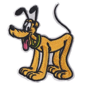 Op de afbeelding: Een geborduurde strijkpatch met een cartoon afbeelding van Pluto, een gele hond met zwarte oren en een groene halsband, staand op alle vier poten met zijn tong naar buiten.