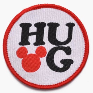 May include: A white round patch with a red border. The patch has black text that says "HUG" with a red Mickey Mouse head in the middle of the "U" and "G".