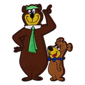 May include: An embroidered patch featuring Yogi Bear and Boo Boo Bear. Yogi Bear is wearing a green hat and a green tie. Boo Boo Bear is wearing a blue bow tie. The patch is brown, green, blue, and yellow.