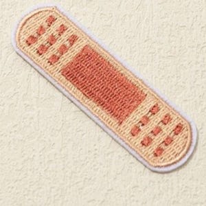 May include: A beige fabric patch with a red embroidered bandage design. The patch has a white border and is ideal for adding a quirky touch to clothing or accessories.