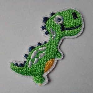 Op de afbeelding: Groene geborduurde dinosaurus patch met witte en gele details. De dinosaurus glimlacht met een blauw oog en een zwarte mond.