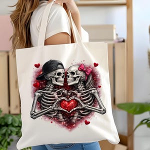 May include: A white tote bag featuring a romantic skeleton couple. The skeletons are embracing, forming a heart with their hands around a red heart. One skeleton wears a black cap, the other a pink bow. Red hearts and glittery accents complete the design.