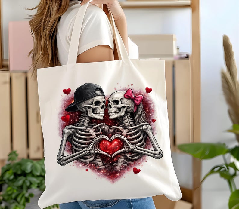 May include: A white tote bag featuring a romantic skeleton couple. The skeletons are embracing, forming a heart with their hands around a red heart. One skeleton wears a black cap, the other a pink bow. Red hearts and glittery accents complete the design.