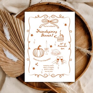 Op de afbeelding: Een Friendsgiving Dinner-uitnodiging met een bruin omtrekdesign op wit papier. De uitnodiging bevat illustraties van een pompoen, taart, kaars en gebraden kalkoen. De tekst luidt "You're Invited to Friendsgiving Dinner!" en "26 november 18.00 uur."