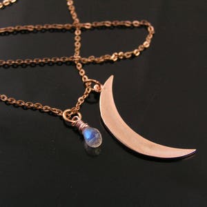 May include: A delicate gold necklace with a crescent moon pendant and a small blue gemstone. The chain is made of small, linked circles.