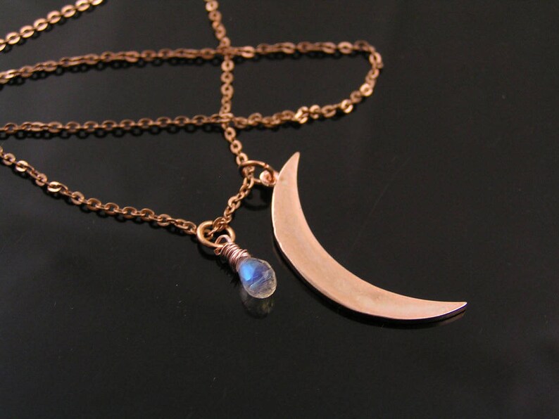 May include: A delicate gold necklace with a crescent moon pendant and a small blue gemstone. The chain is made of small, linked circles.