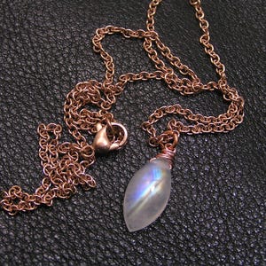 May include: A rose gold chain necklace with a teardrop-shaped iridescent moonstone pendant.