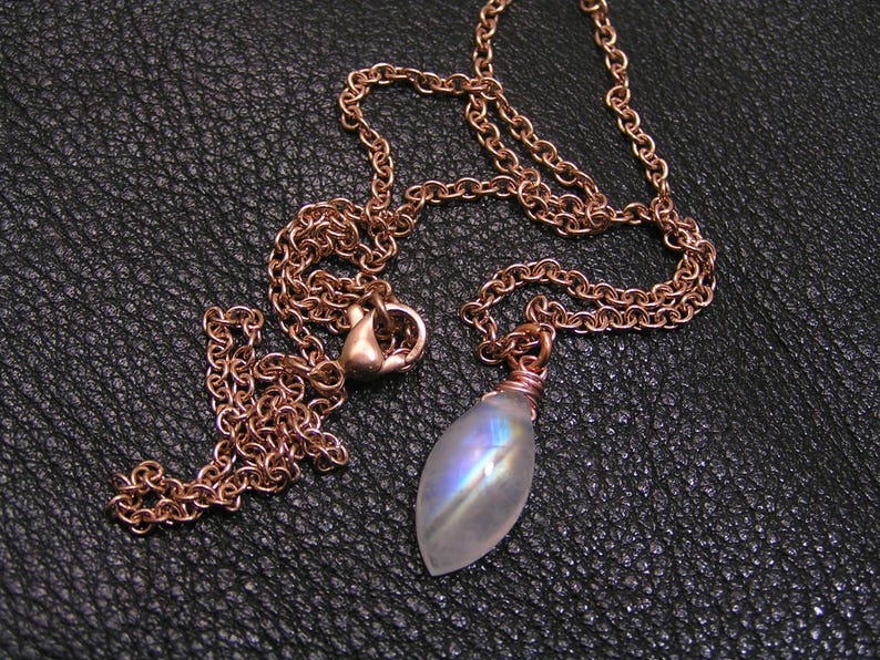 May include: A rose gold chain necklace with a teardrop-shaped iridescent moonstone pendant.