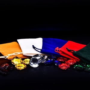 May include: Five velvet drawstring pouches in brown, orange, white, blue, and green, with a variety of colorful gemstones scattered in front of them.