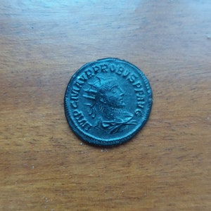 Könnte beinhalten: Eine schwarze Metallmünze mit dem Profil einer Person, die eine Krone trägt, und dem Text "IMP. CAESAR. PROBUS. AVG."